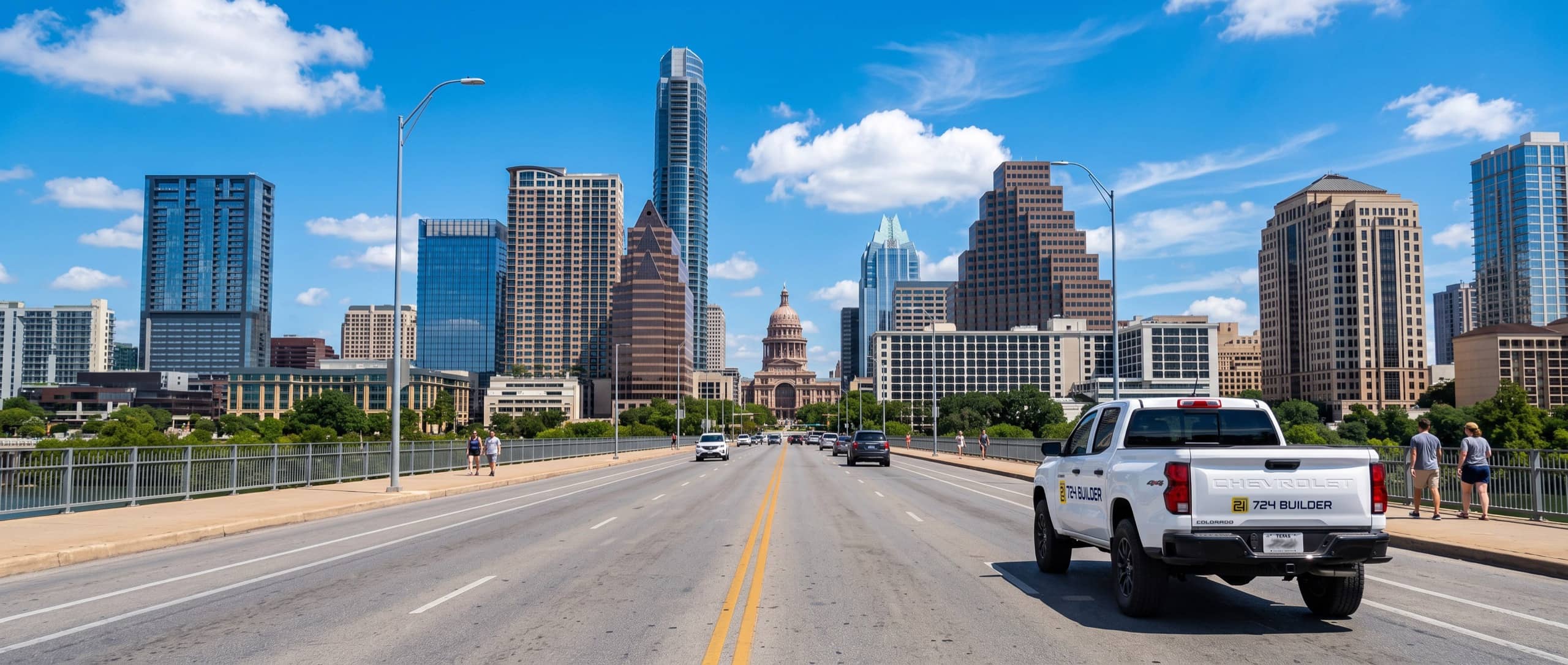 A view north along Congress Avenue from the Congress Avenue Bridge in Austin under a bright blue sky, the downtown skyline rising on both sides and the domed Texas State Capitol at the far end of the street, with a 724 Builder pickup in the right-hand lane heading toward it.